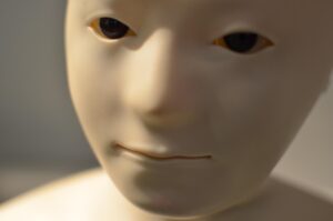 Twarz humanoida z jasnego tworzywa, z ruchomymi oczami i zarysem uśmiechu, w zbliżeniu