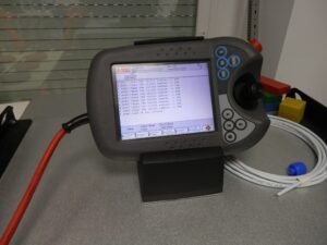 Ręczny panel programowania robota ABB (teach pendant) z joystickiem i przyciskiem awaryjnym, na ekranie komunikaty programu
