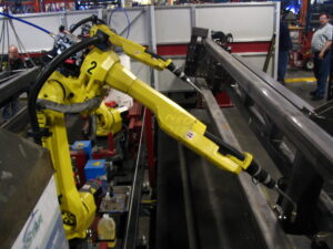 Spawalniczy robot przemysłowy FANUC przy stalowej belce w hali produkcyjnej