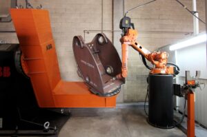 Robot spawalniczy ABB z palnikiem obok dużego pomarańczowego pozycjonera, który trzyma spawaną stalową konstrukcję