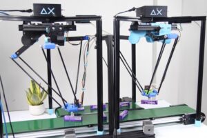 Dwa roboty typu delta nad przenośnikiem taśmowym przekładające produkty