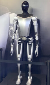 Robot Tesla Optimus na wystawie: srebrna obudowa, czarna głowa bez twarzy