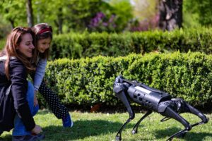Robot pies Unitree na trawniku, obok zaciekawiona kobieta z dzieckiem